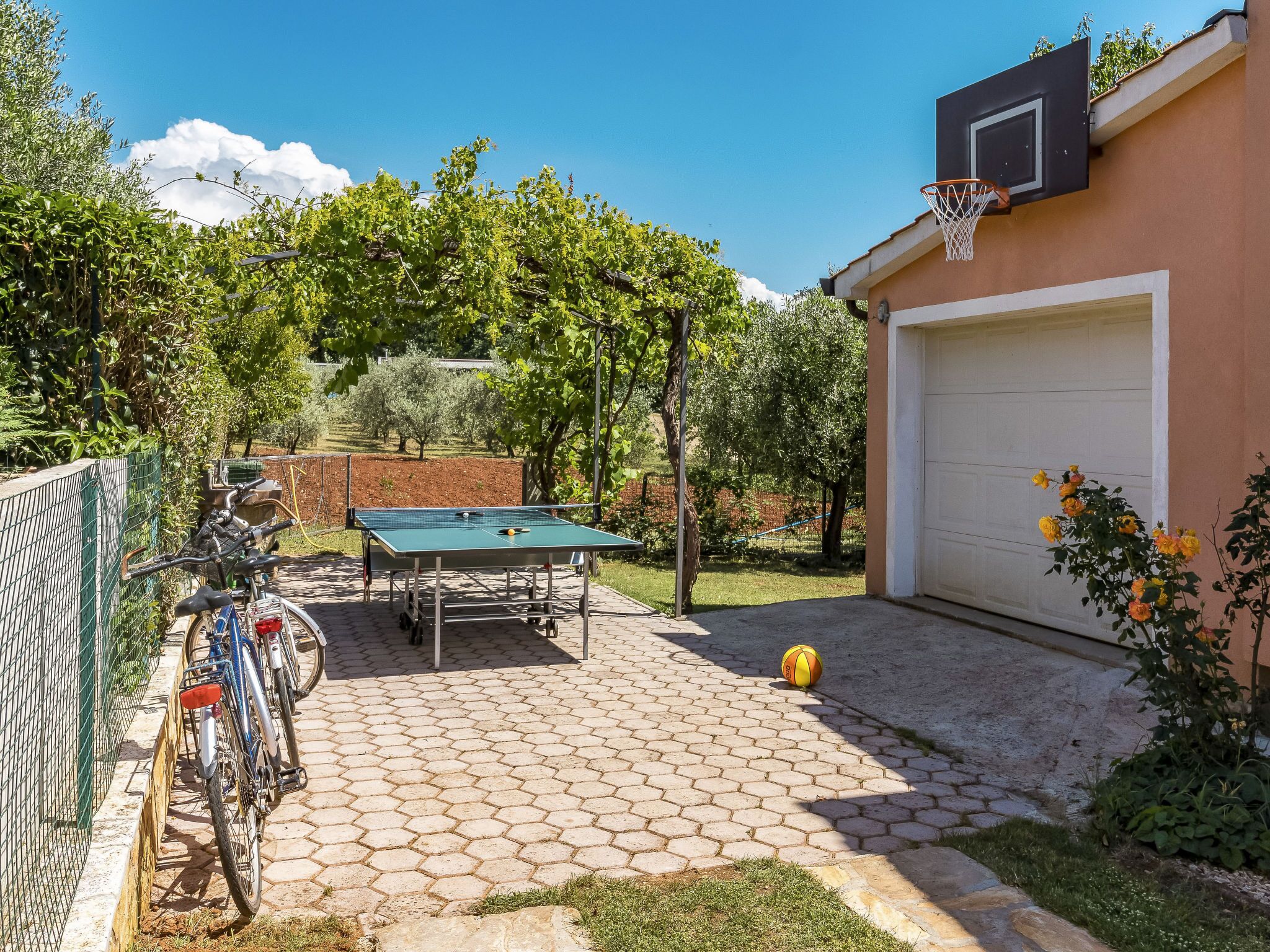A backyard with a ping pong table, a bicycle, and a basketball hoop.