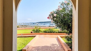 Vista a través de un arco hacia un puerto deportivo con barcos, un área verde y una planta floreciente.