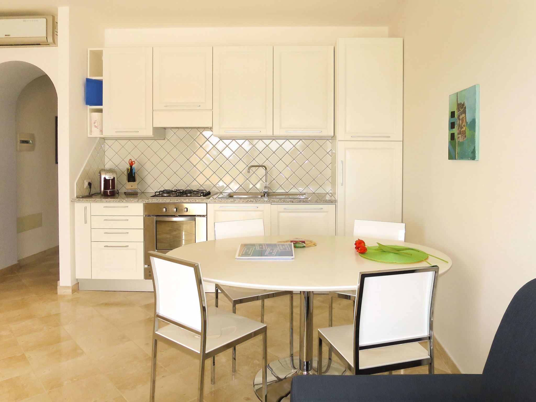 Una cocina compacta con armarios blancos, una estufa a gas y un comedor con una mesa redonda y sillas.