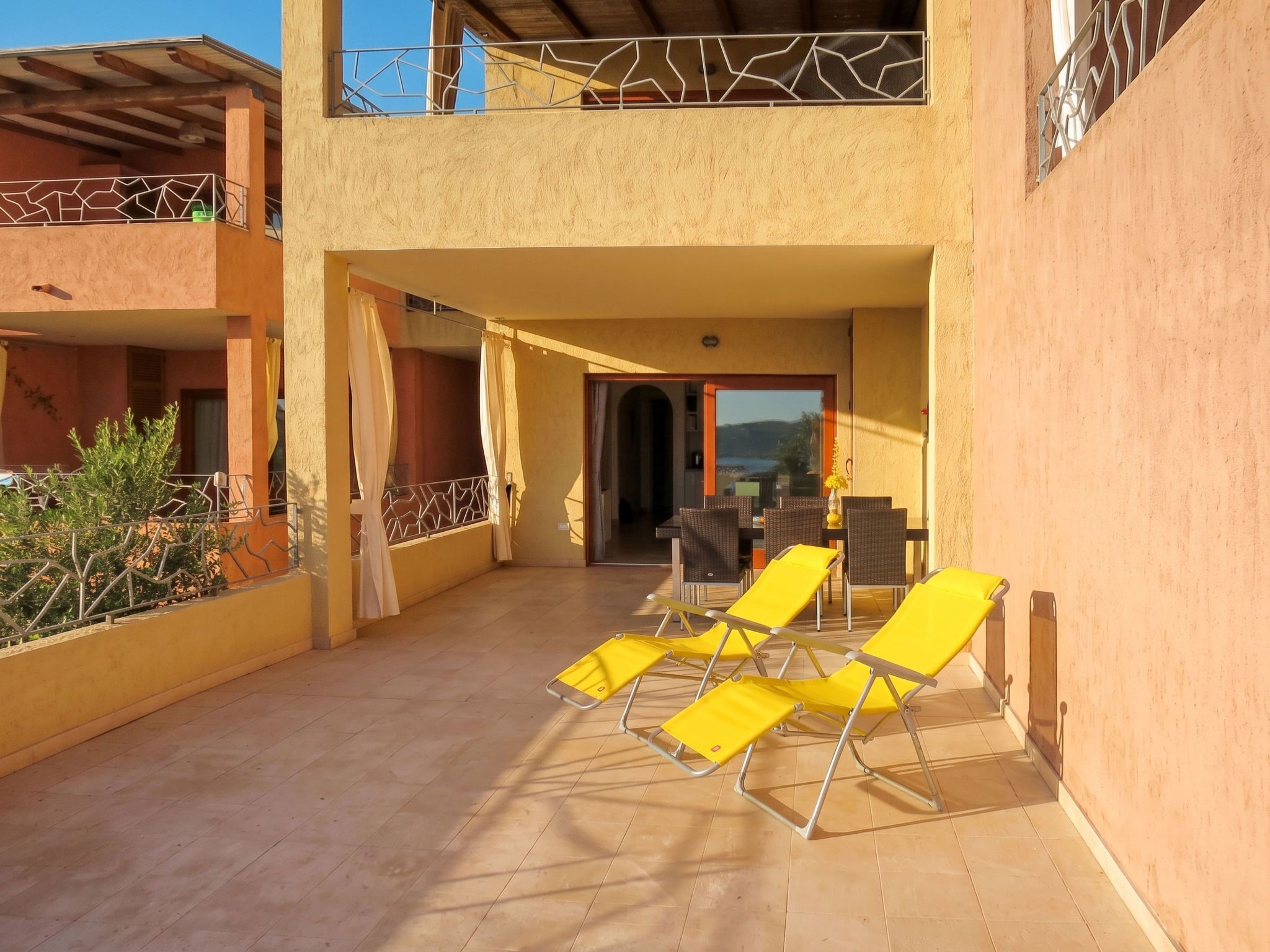A covered outdoor area with yellow lounge chairs, a dining table, and a view of the sea.