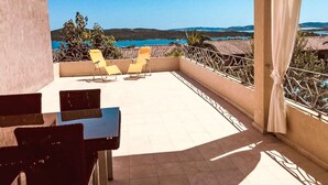 Un balcon avec deux chaises jaunes, une table et une vue sur la mer et les collines.
