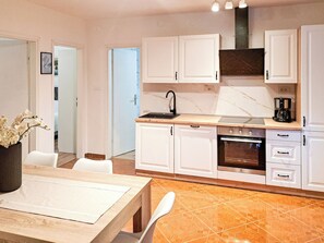 Una cocina moderna con armarios blancos, horno empotrado y cafetera.