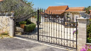 A gated entrance with a wrought iron gate, a stone wall, and a building with a tiled roof. - Glavica by Interhome (Poreč)