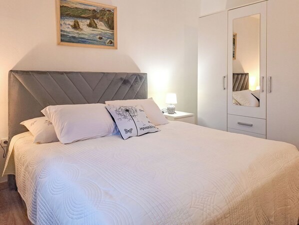 Una cama bien hecha con cubrecama acolchada, cabecera y mesita de noche con lámpara.