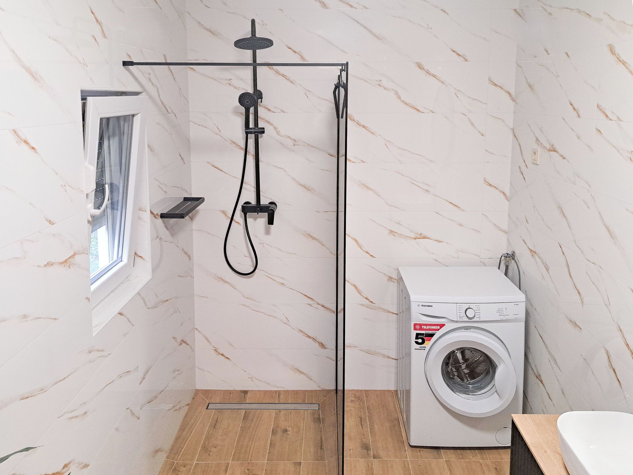 A compact bathroom with a shower, a window, and a washing machine.
