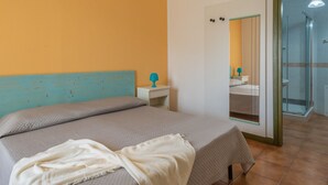 Un dormitorio con cama, mesita de noche, espejo y baño visible a través de una puerta de vidrio.