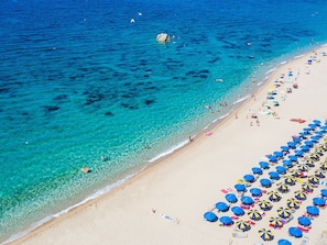 A beach with clear turquoise water, a sandy shore, and numerous blue and yellow umbrellas. - Camping Village Baia Blu La Tortuga by Interhome (Vignola Mare)