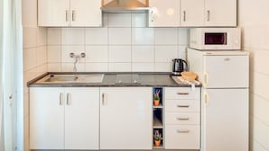 A compact kitchen with white cabinets, a stainless steel range hood, a microwave, and a refrigerator. - Apartment Kuki by Interhome (Poreč)