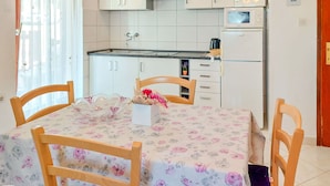 A kitchen with white cabinets, a stainless steel range hood, a microwave, and a refrigerator. There is a dining table with chairs and a floral tablecloth. - Apartment Kuki by Interhome (Poreč)