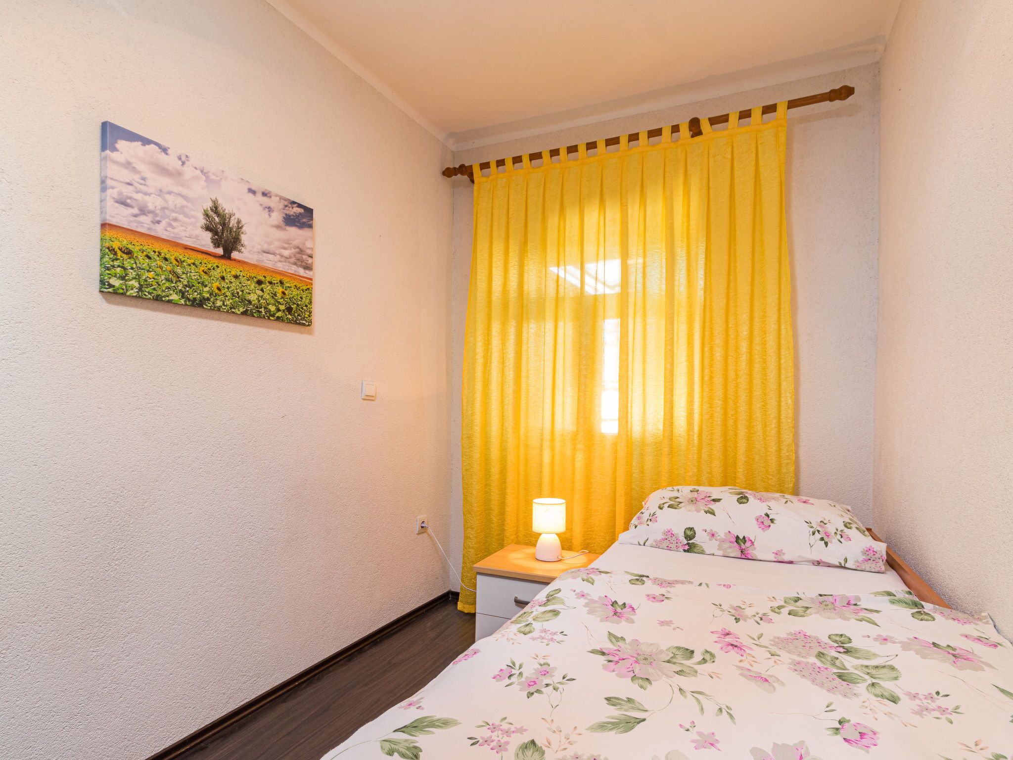 Une chambre à coucher avec un lit, une table de chevet, une lampe, un tableau et un rideau jaune.