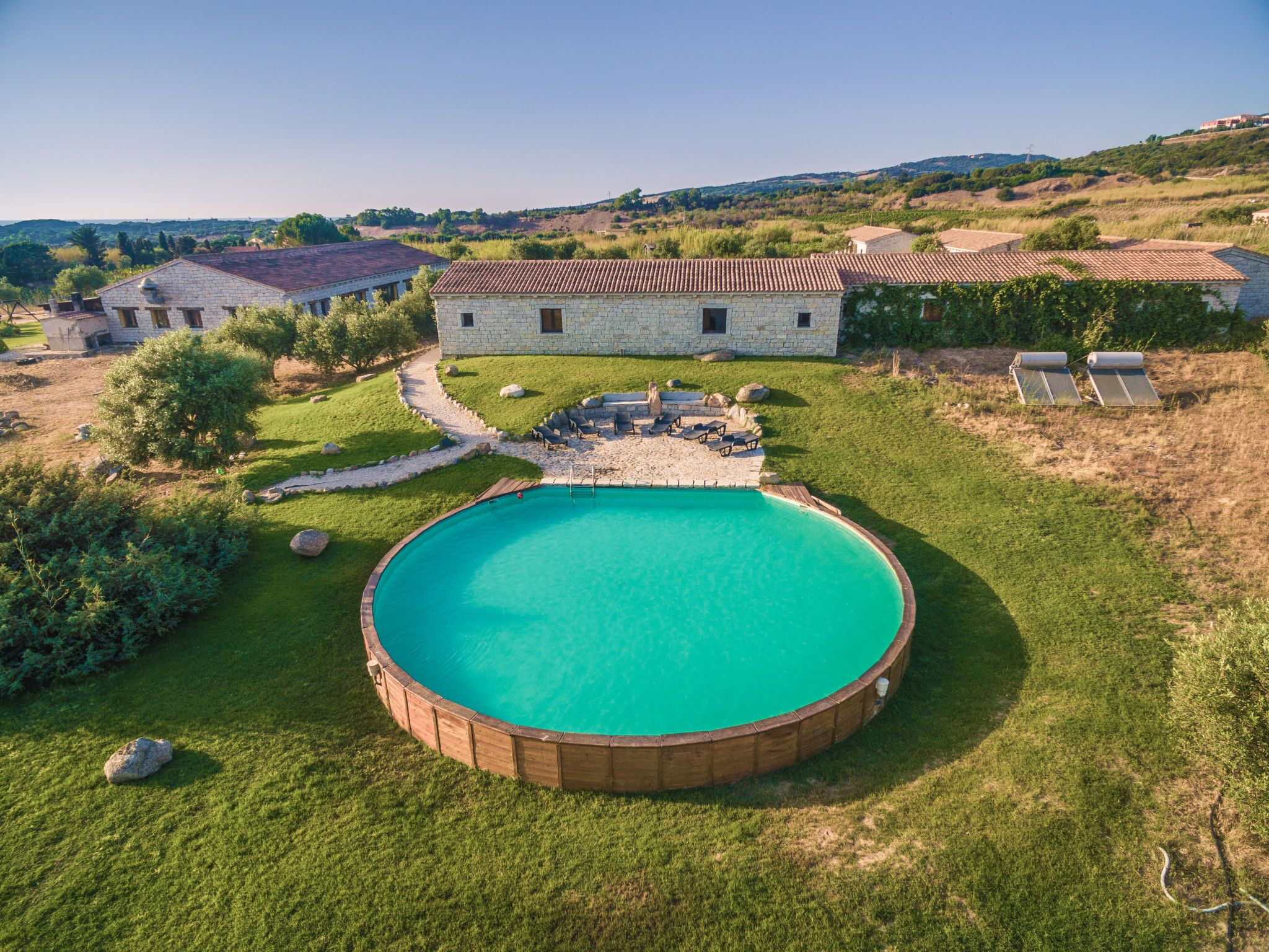 A stone house with a swimming pool surrounded by a wooden deck and lounge chairs.