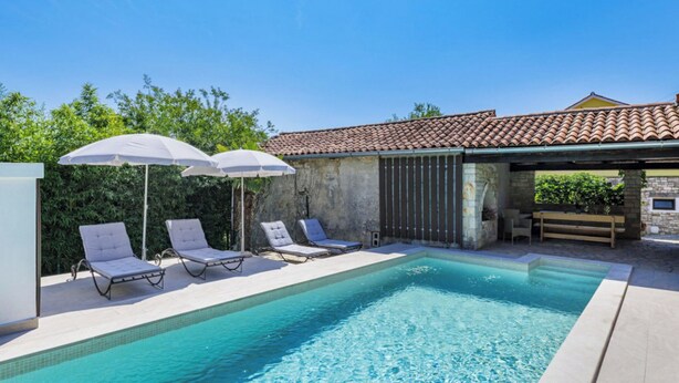A swimming pool with lounge chairs and umbrellas, surrounded by a stone wall and a tiled roof structure. - Vacation home Kate by Interhome (Pićan)