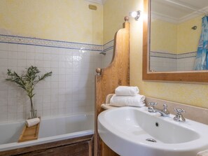 A bathroom with a bathtub, a sink, a mirror, and a decorative plant.