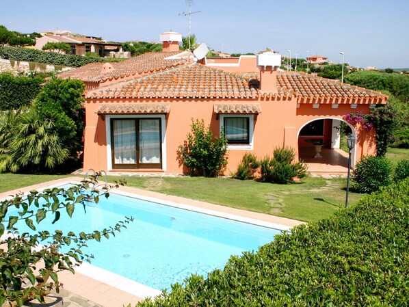 A house with a swimming pool, surrounded by greenery and a clear sky.