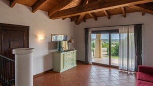 Une pièce spacieuse avec un plafond en bois, une porte-fenêtre coulissante donnant sur un balcon, un meuble de couleur claire et un fauteuil rouge.