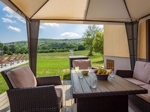 Relax on the patio with a view of the lush green landscape, surrounded by wicker furniture and a shaded seating area.