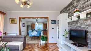 Ein modernes Wohnzimmer mit Flachbildfernseher, Holzboden und Essbereich im Hintergrund.