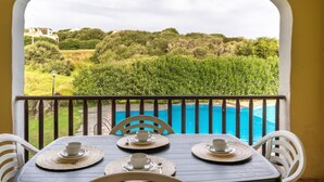 Ein Balkon mit Tisch für zwei Personen, Blick auf einen Pool und üppige Bepflanzung.