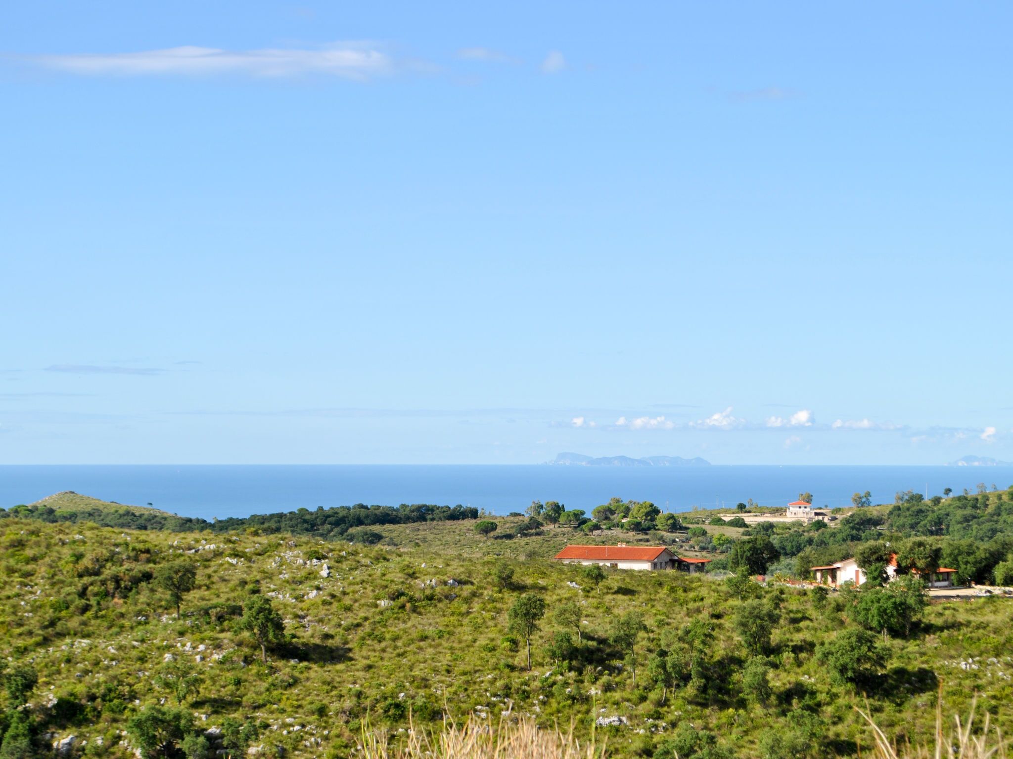 A rural landscape with scattered houses, a clear sky, and a distant view of the sea.