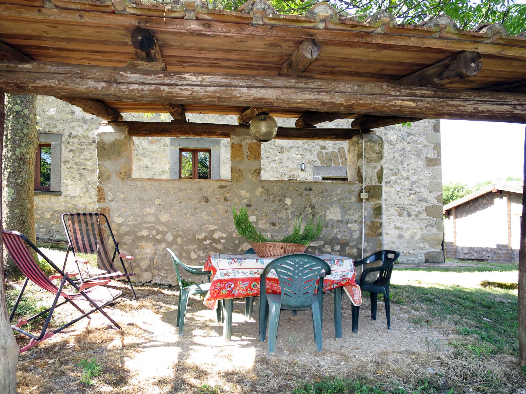 An outdoor patio with a rustic stone wall, wooden pergola, and a table set for dining.