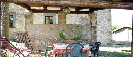 An outdoor patio with a rustic stone wall, wooden pergola, and a table set for dining.