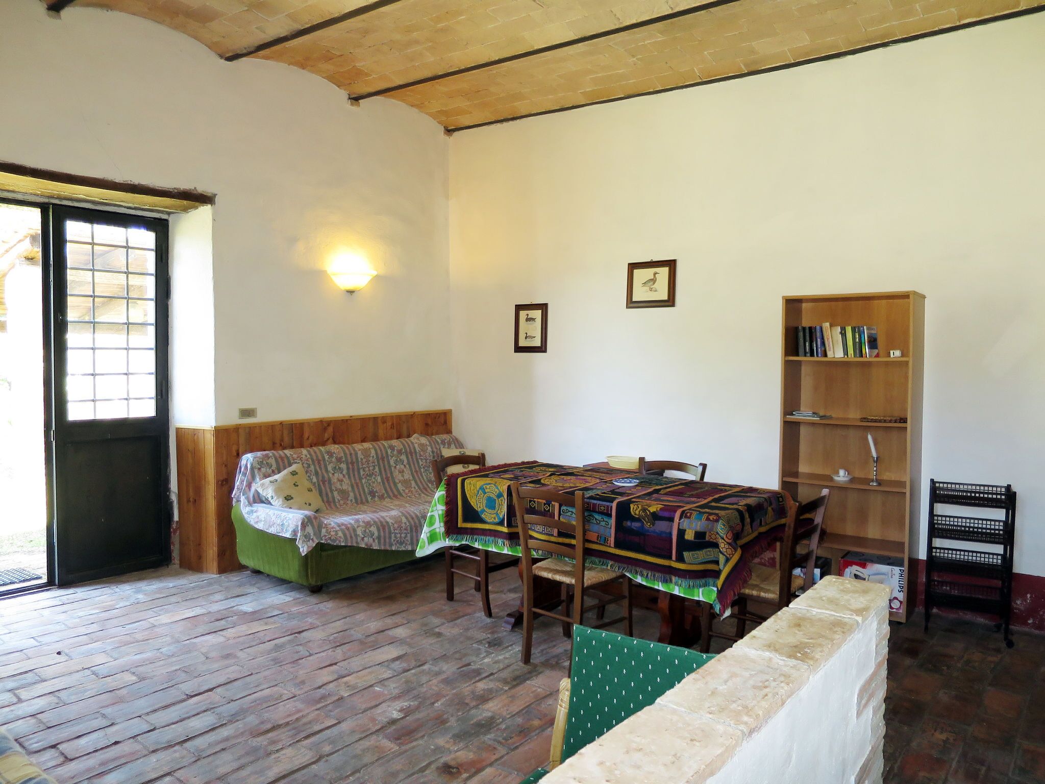 A cozy room with a wooden floor, a green sofa, a dining table with chairs, a bookshelf, and a door with a window.