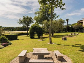 Un jardin bien entretenu, agrémenté d’une table de pique-nique et de bancs, entouré de haies et d’arbres taillés avec soin.