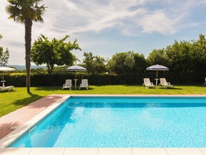 Une piscine entourée de verdure, avec des chaises longues et des parasols.