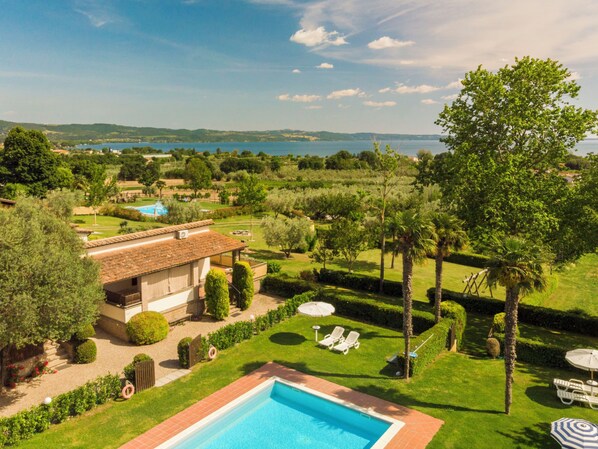 A pool with a view of the sea, a house with a tiled roof, and a well-maintained garden.