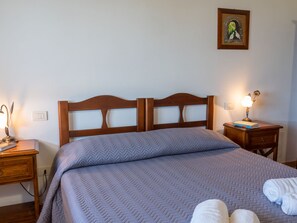 A neatly made bed with a wooden headboard, a bedside table with a lamp, and a small bedside table with a book and a lamp.