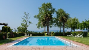 A rectangular swimming pool with a metal ladder, surrounded by a well-maintained lawn and trees.