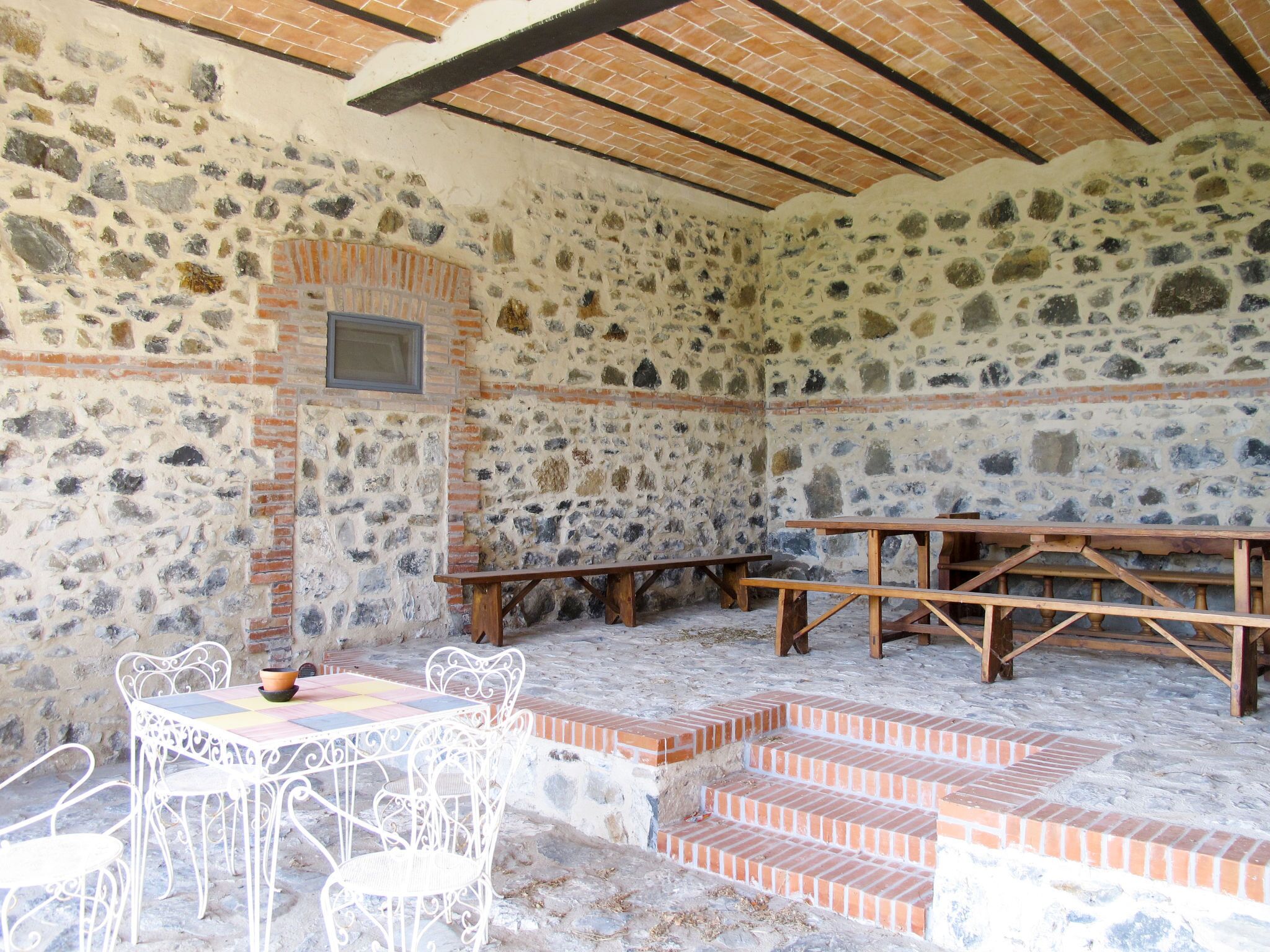 A stone-walled room with a tiled floor, a wooden bench, and a small table with chairs.