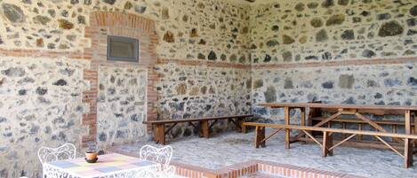 A stone-walled room with a tiled floor, a wooden bench, and a small table with chairs.