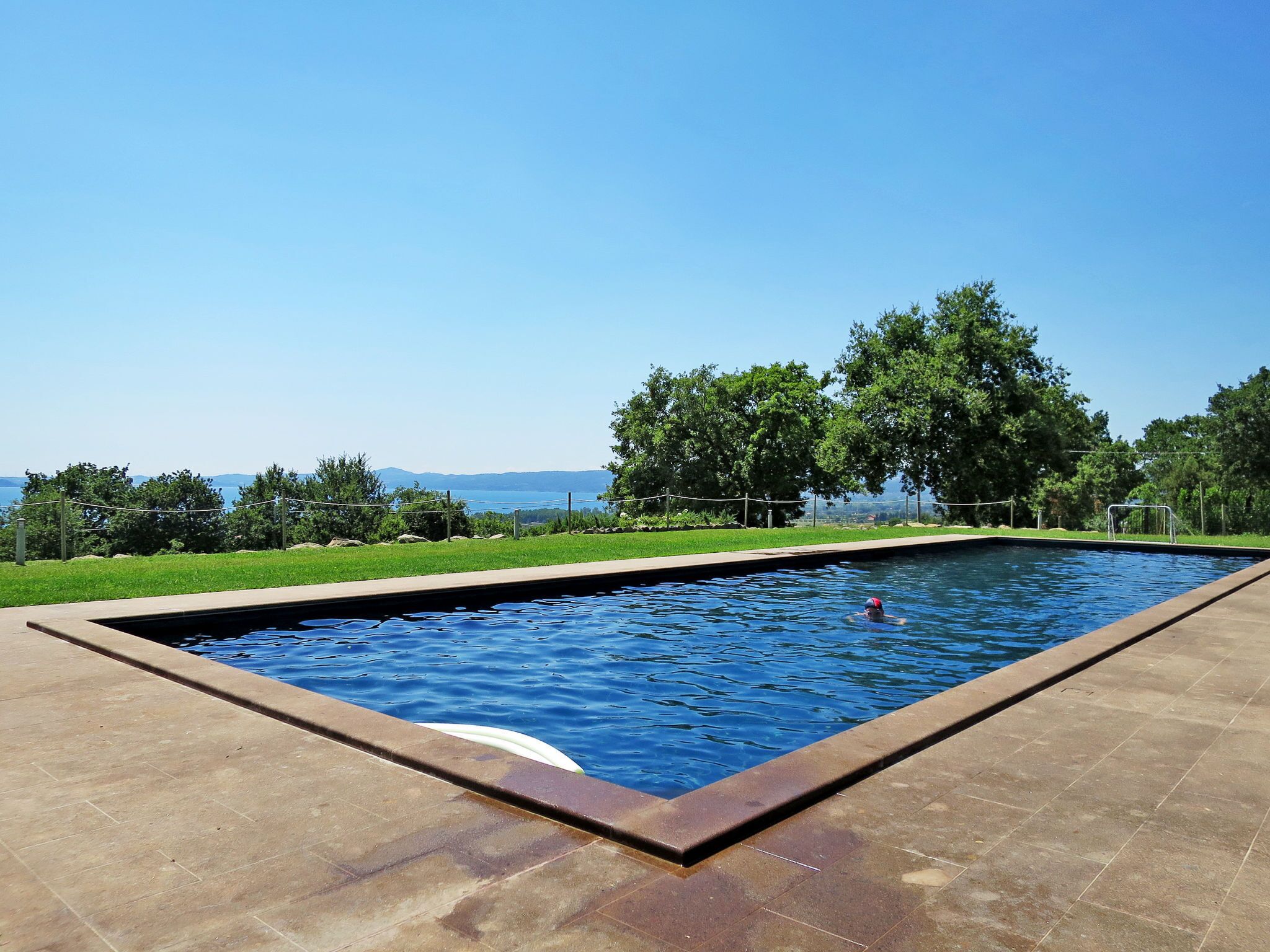 A rectangular swimming pool with a clear view of the surrounding landscape, including trees and a distant body of water.