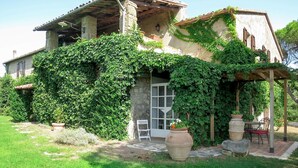 Une maison de campagne aux murs recouverts de lierre, dotée d’une cheminée en pierre et d’une pergola en bois avec des sièges pour l’extérieur.