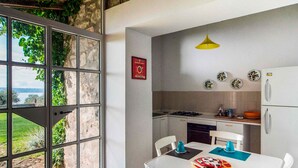 Une cuisine donnant sur un espace verdoyant, une table à manger avec des chaises, une lampe suspendue jaune et un panneau accroché au mur.