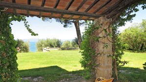 Une chaise en osier placée sous une pergola, avec vue sur une zone herbeuse et un plan d’eau.