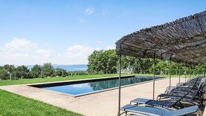 En rektangulär swimmingpool med en pergola och solstolar.