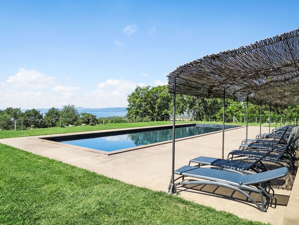 A rectangular swimming pool with a pergola and lounge chairs.