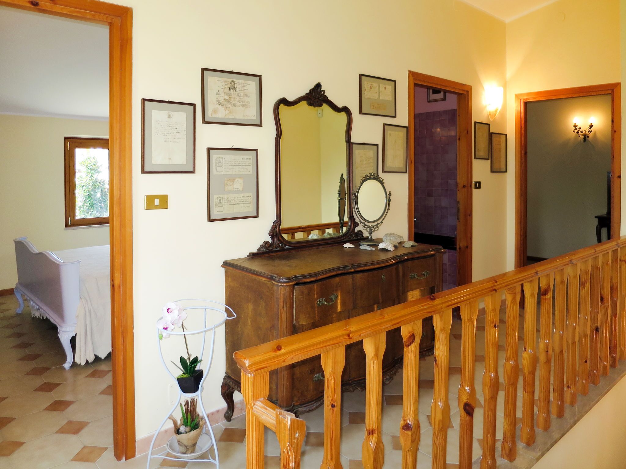 A staircase with a wooden handrail, a wooden dresser with a mirror, and several framed certificates on the wall.