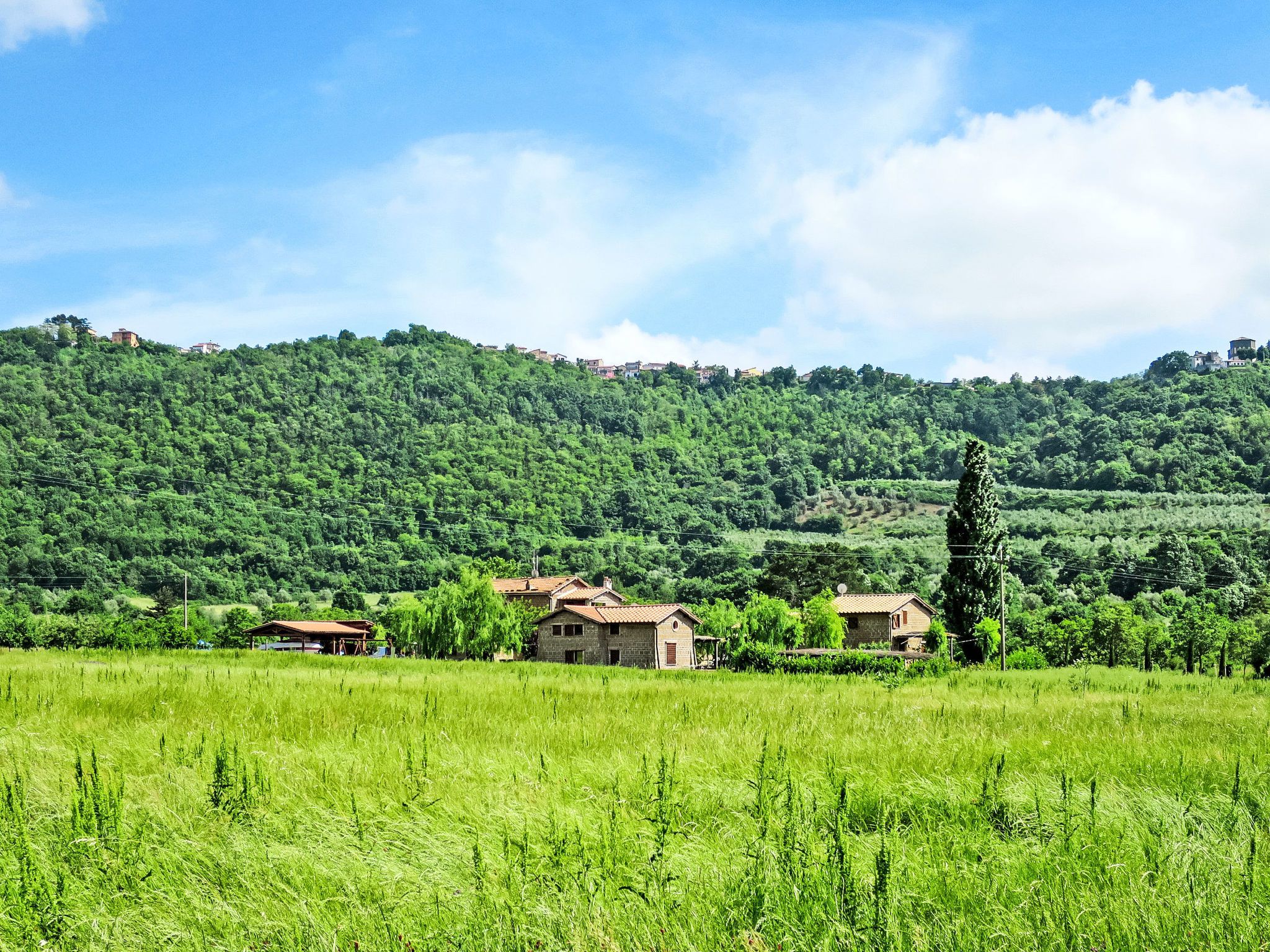 Un paysage rural avec des maisons sur une colline, un ciel dégagé et un champ au premier plan.