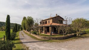 Une maison de campagne en pierre, avec un toit en tuiles, entourée d’une allée de gravier et d’une végétation luxuriante.