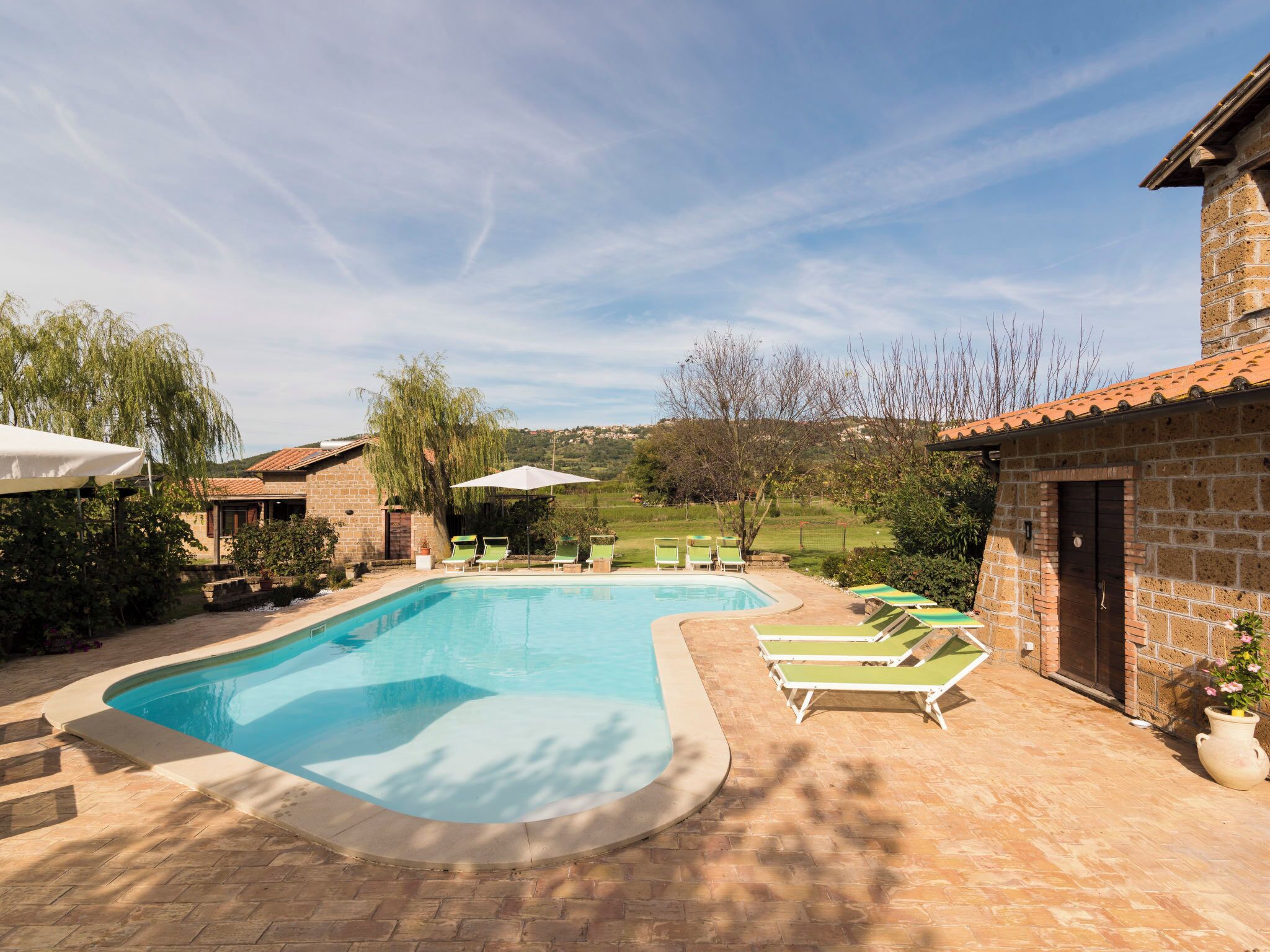A swimming pool with a curved edge, surrounded by lounge chairs and umbrellas.