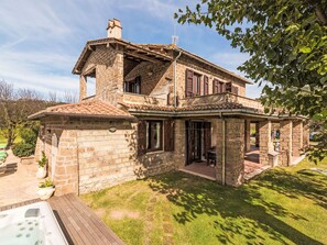 A stone house with a tiled roof, a wooden deck, and a garden area.