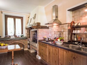 A kitchen with a brick fireplace, wooden cabinets, and a tiled backsplash. - Casa Domenico n° 1 by Interhome (Lago di Bolsena)