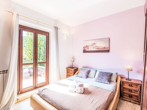 A bedroom with a bed, two bedside tables, a painting, and a window with curtains.