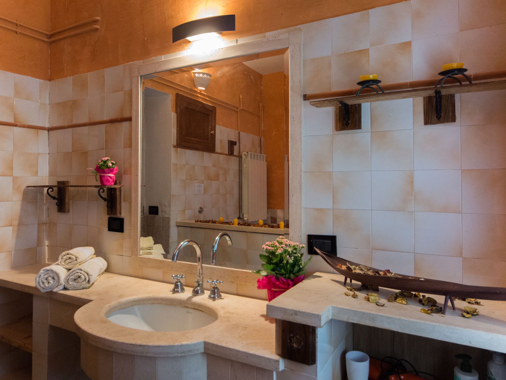 A modern bathroom with a large sink, two faucets, a mirror, and a shelf with toiletries.