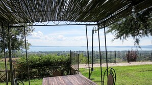 A covered outdoor seating area with a table and chairs, overlooking a scenic landscape with a body of water and distant mountains.