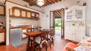 A kitchen with wooden cabinets, a dining table with chairs, and a white cabinet with glass doors. - Alighiero II by Interhome (Boccheggiano)
