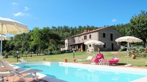 A swimming pool with lounge chairs and umbrellas, surrounded by a stone building and greenery. - Alighiero II by Interhome (Boccheggiano)
